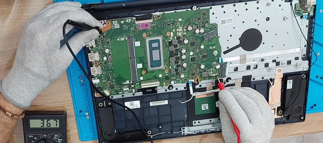 Manos con guantes midiendo una placa de notebook con las puntas de un multímetro