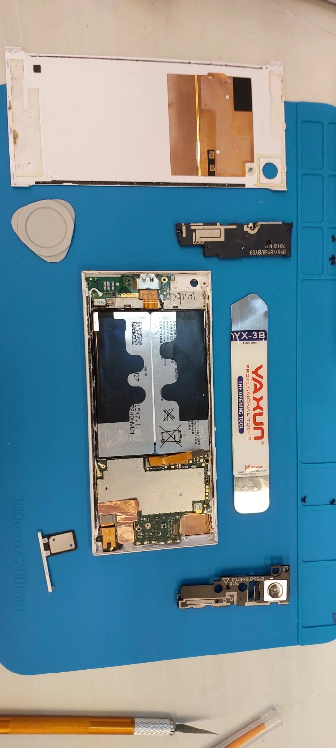 Celular abierto sobre una base azul junto a la tapa y componentes desmontados
